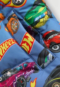 Modrá látka s farebnými dizajnmi karikatúrnych áut a vzormi plameňov, s viditeľnými nášivkami a stehy, vytvárajúcimi textúrovaný vzhľad.