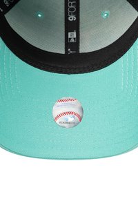 Türkisfarbene Baseballmütze mit schwarzem Schirm, auf der Innenseite mit einem runden MLB-Logo-Aufkleber. Strukturierter Stoff, strukturiertes Design.