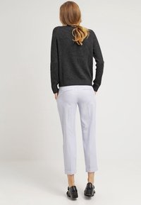 Sweter z dzianiny w kolorze węgla, zestawiony z jasnoszarymi spodniami w wzory, mającymi proste nogawki i mankiety, uzupełniony czarnymi butami.