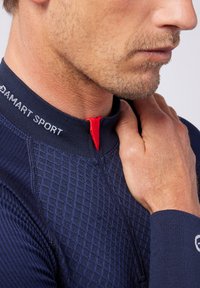 Marine thermische sporttop met een getextureerd ruitpatroon, ritssluiting met rode accentkleur en aansluitende lange mouwen. Merkenlogo op de kraag.