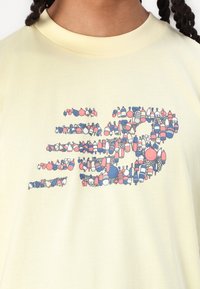 Jasnożółta koszula z grafiką czerwonych, niebieskich i białych bojek wędkarskich ułożonych w poziomy wzór na klatce piersiowej.