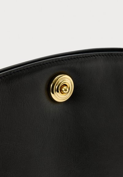 Crna kožna površina s detaljno zlatnom kružnom magnetskom kopčom, prikaz blizu.