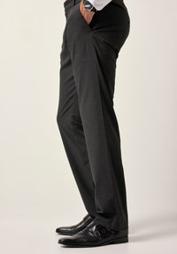 Pantalones grises a medida hechos de tela texturizada. Cuentan con bolsillos laterales y un diseño ajustado, combinados con zapatos de vestir negros brillantes.