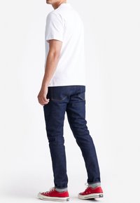 Witte katoenen t-shirt, donkerblauwe spijkerbroek en rode kanvas sneakers. Zichtbare stiksels en klassieke ontwerpelementen. Eenvoudige, casual outfit.