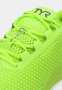 Neonowo zielone buty sportowe z siateczkową teksturą, z wyściełanym językiem, wzmocnionymi oczkami i detalem z logo; posiadają zintegrowane sznurowadła zapewniające pewne dopasowanie.
