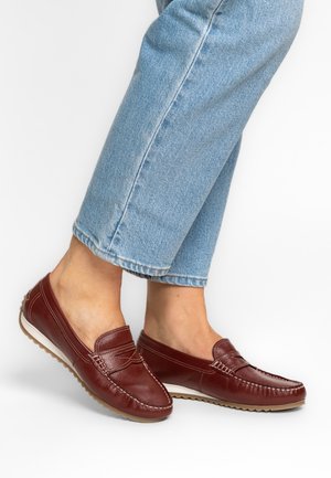 Person trägt hellblaue, gekürzte Jeans und dunkelrote Leder-Slipper mit weißer Sohle.