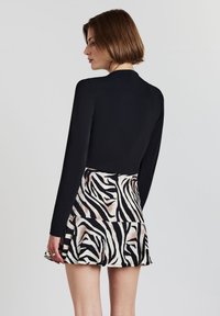 Schwarzes Langarmtop mit hohem Kragen, kombiniert mit einem kurzen Rock mit einem Zebra-Streifenmuster in Schwarz und Beige.