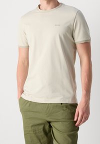 T-shirt corto a maniche corte color beige chiaro in cotone con colletto e polsini a coste; presenta il sottile logo "BOSS" sul petto.