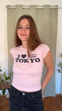 Rožinė medvilninė trumparankovė marškinėliai su juodu užrašu: „I ❤️ 〒 100-0011, Japonija Tokijas.“ Derinama su tamsios spalvos džinsine suknele.