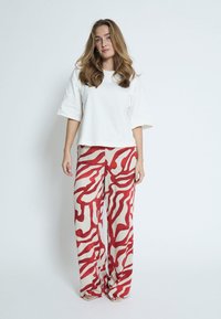 Weißes, übergroßes T-Shirt mit kurzen Ärmeln, kombiniert mit lockeren, gemusterten Hosen in Rot und Creme mit wellenförmigen Linien. Glatte Stoffstruktur.