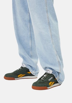 Grüne und gelbe Wildledersneaker mit Gummisohlen, Schnürsenkeln und Logodetail. Getragen zu lockeren, hellblauen Jeans.