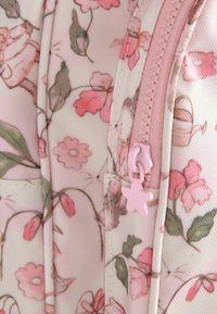 Gros plan d'un tissu rose avec des motifs floraux et papillons et un curseur de fermeture éclair rose en forme d'étoile.