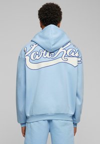 Light blue hoodie featuring a large white script logo on the back, with a drawstring hood and ribbed cuffs and hem. Smooth texture.