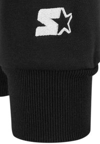 Black cotton fabric with ribbed texture featuring a white embroidered logo and star design. The bottom hem is also ribbed.