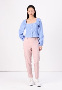 Lyseblå stripete skjorte med knapper og puffede ermer, kombinert med rosa skreddersydde bukser og hvite joggesko. Enkel, moderne design.