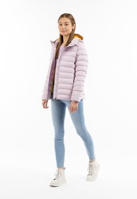 Giacca puffer viola chiaro con cappuccio, caratterizzata da cuciture orizzontali e foderata internamente di giallo. Abbinata a jeans skinny blu chiaro e sneaker bianche.