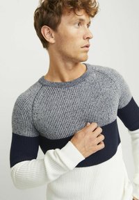 Pulover tricotat cu un design în blocuri de culoare în gri, bleumarin și alb. Textură cu caneluri, guler rotund și mâneci lungi.