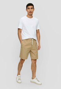 Beige Baumwollshorts mit einem Kordelzugbund und seitlichen Taschen, kombiniert mit einem schlichten weißen T-Shirt und weißen Sneakern.