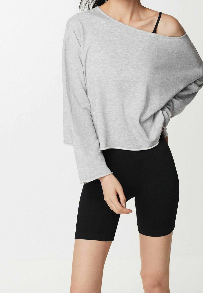 Haut gris à manches longues raccourci avec un design épaule dénudée, associé à un short cycliste noir moulant. Le tissu semble doux et extensible.