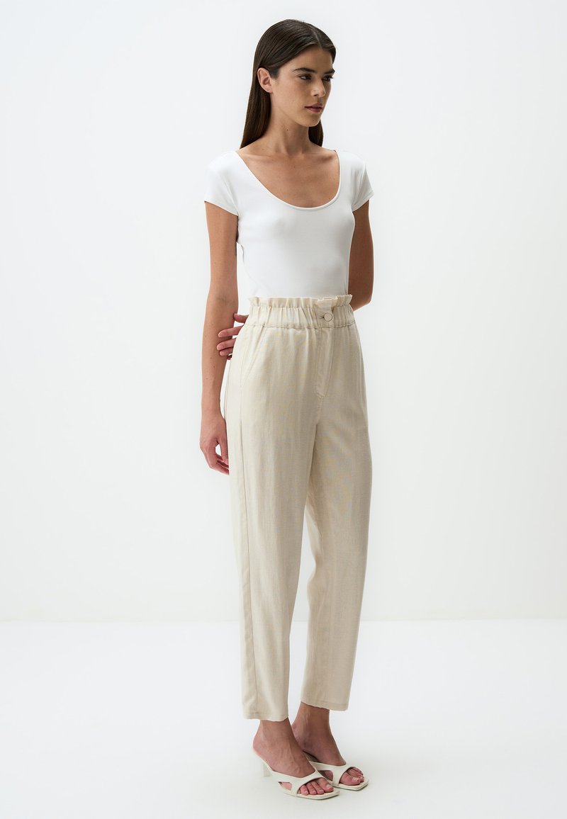 Haut blanc ajusté avec un décolleté plongeant, associé à un pantalon beige taille haute avec une taille froncée et un détail de bouton.
