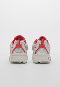 Ett par vita och röda träningssneakers sedd bakifrån, med mesh-tyg, vadderade sulor och hälltappar vid hälen.