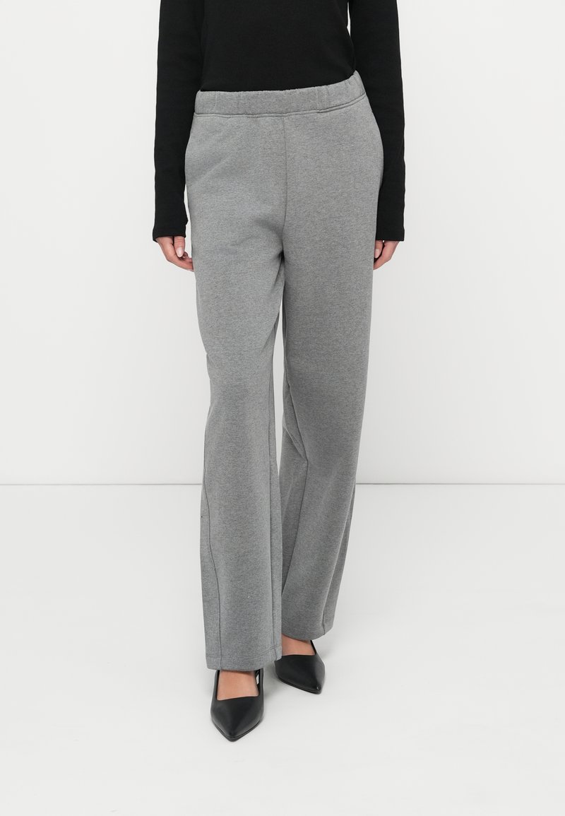 Grå joggingbukser med afslappet pasform, elastisk talje og lige ben, kombineret med sorte spidse hæle. Glat tekstur, minimalistisk design.