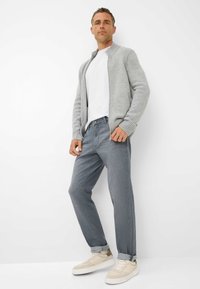 Cardigan grigio lavorato a maglia sopra una maglietta bianca, abbinato a jeans grigio chiaro e sneaker beige. Texture liscia e vestibilità casual.