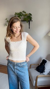 Biely rebrovaný crop top so štvorcovým výstrihom, v kombinácii s modrými džínsami s vysokým pásom. Jednoduchý dizajn s krátkymi rukávmi a jemným kvetinovým vzorom.