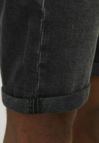 Zwarte denim shorts met een opgerolde zoom, met een soepele textuur en subtiele vervaging, met gedetailleerd stikwerk langs de naden.