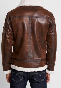 Bruine leren jas met een shearling kraag en manchetten, met een gladde textuur en contrasterende donkere leren accenten.