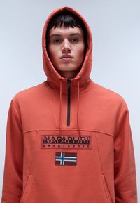 Felpa con cappuccio arancione realizzata in tessuto morbido, con collo zip, un logo patch frontale e un dettaglio ricamato della bandiera norvegese.
