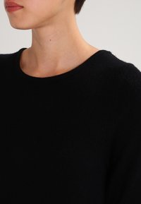 Maglione nero con scollo rotondo, texture morbida e maniche corte. Il design presenta uno stile semplice e una forma aderente.