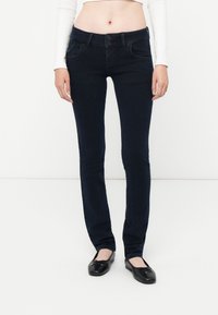 Jeans oscuros de corte ajustado, hechos de tela de mezclilla. Cuentan con una bragueta de botones, bolsillos frontales y una textura suave.