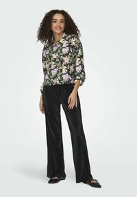 Apkarpyta juoda gėlėta palaidinė su violetinėmis ir kremine gėlėmis ant žalio fono, derinama su juodais plačiomis pėdomis ir klostuotais kelnėmis. Juodi batai.