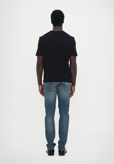 Zwarte t-shirt met korte mouwen gecombineerd met blauwe denim jeans. De jeans hebben een lichte wassing en zijn taps toelopend bij de enkels, wat goed past bij de zwarte schoenen.