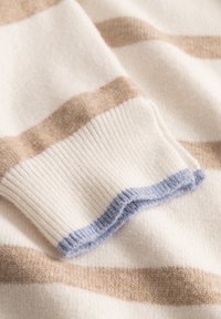 Sweter wełniany w kremowo-beżowe paski, z prążkowanymi mankietami. Mankiety mają miękki niebieski akcent. Tkanina wydaje się teksturowana i przytulna.