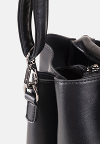 Schwarze Lederhandtasche mit abnehmbarem Tragegurt, befestigt an silbernen Metallringen, mit offenem oberen Teil und sichtbarer Reißverschlusstasche innen.