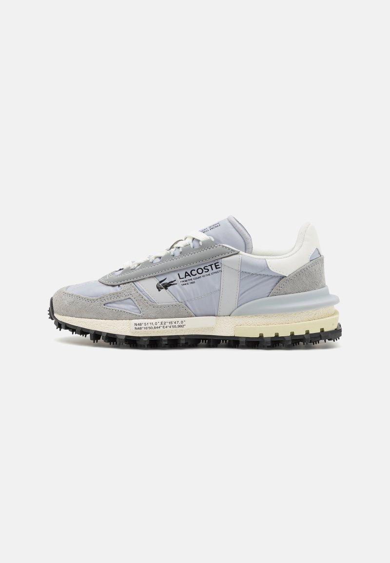 Világosszürke sneaker, sima bőrből és velúrból készült, textúrázott részletekkel, fehér sarokkal és fekete gumitalppal, ami tüskés.