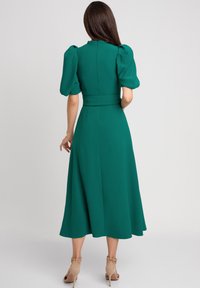 Zielona sukienka midi z puff sleeves, dopasowaną talią, zwiewnym dołem i gładką strukturą materiału. Posiada zamek błyskawiczny z tyłu oraz skromny dekolt.