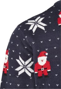 Pull en tricot bleu marine avec des flocons de neige blancs et des figures de Père Noël rouges. Tissu texturé avec des motifs complexes et des couleurs contrastées.
