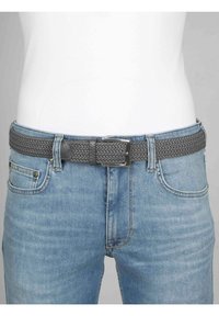 Grau gewebter Gürtel mit einer Metallschnalle, kombiniert mit hellblauen Jeans. Der Gürtel verfügt über ein strukturiertes Muster und einen glatten Lederakzent.