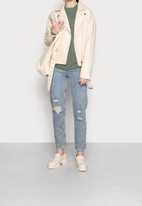 Cremfarbene Lederjacke im Übergröße-Stil, grüner Strickpullover, ausgewaschene blaue Jeans und klobige beigefarbene Slippers.
