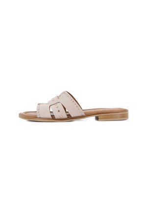 Sandalia beige tipo slide con tiras anchas de ante con tachuelas doradas y un tacón bajo de madera apilada, mostrada de perfil.