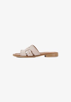 Sandalia beige tipo slide con tiras anchas de ante con tachuelas doradas y un tacón bajo de madera apilada, mostrada de perfil.