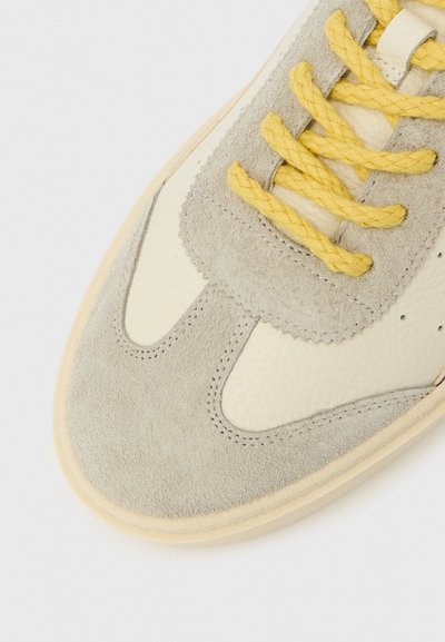 Tossud, millel on hall seemisnahast ninaosa, kreemjas nahast detailid, kollased tekstuuriga paelad ja pehme kreemjas tald. Minimaalne disain.