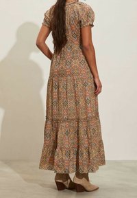 Maxi šaty vyrobené z vzorované tkaniny s krátkými puff rukávy, stahovaným pasem a vrstvenou sukní; barvy zahrnují rezavou, modrou, zelenou a krémovou.