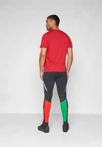Camiseta corta roja de manga corta combinada con leggings negros ajustados que presentan vibrantes acentos rojos y verdes, y detalles laterales reflectantes.