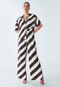 Brown and cream striped two-piece outfit featuring a short-sleeve button-up shirt and wide-leg pants with an elastic waist. Smooth fabric texture.