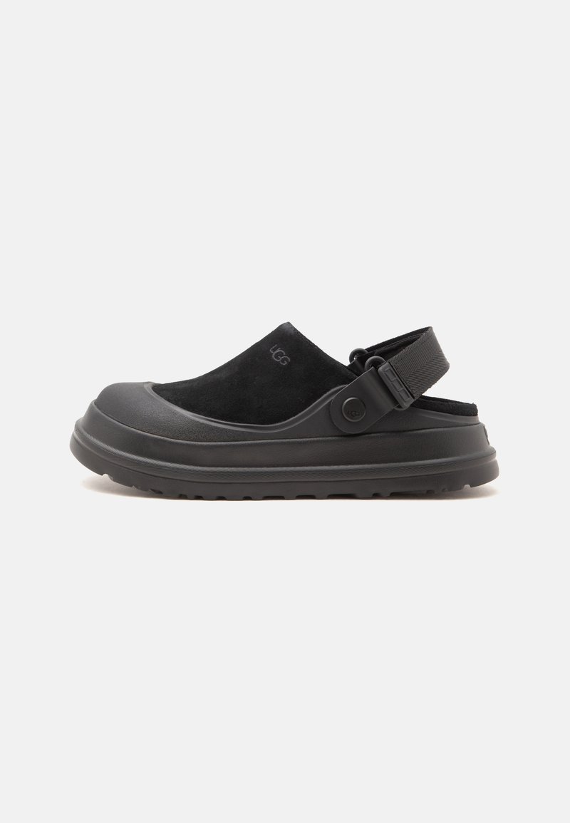 Sabot noir à enfiler avec bride arrière réglable, semelle épaisse et dessus en daim avec un logo discret de la marque sur le côté.