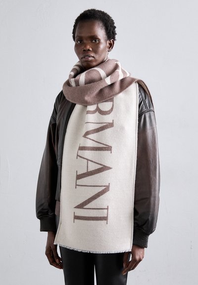 Écharpe en mélange de laine avec une base crème clair ornée du texte "ARMANI" en marron, drapée autour du cou, associée à une veste bomber en cuir noir.